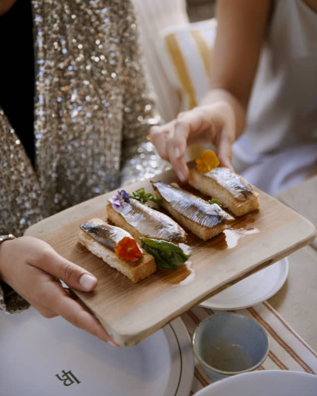 Close-up of the dinner table as guests pass round a board of flower-garnished sardine fillet starters at Tramuntana Grill.