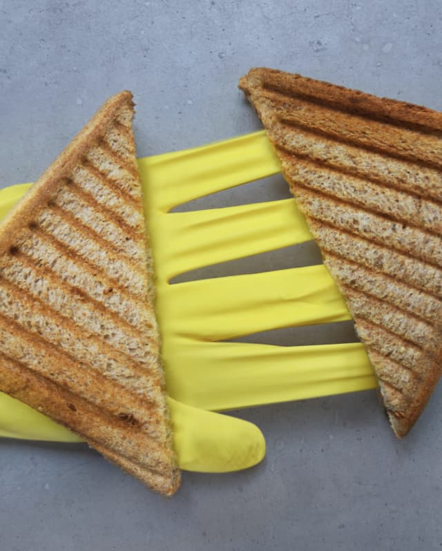 Two triangles of grilled toast lay facing each other on the palm and fingers of an outstretched yellow washing-up glove.