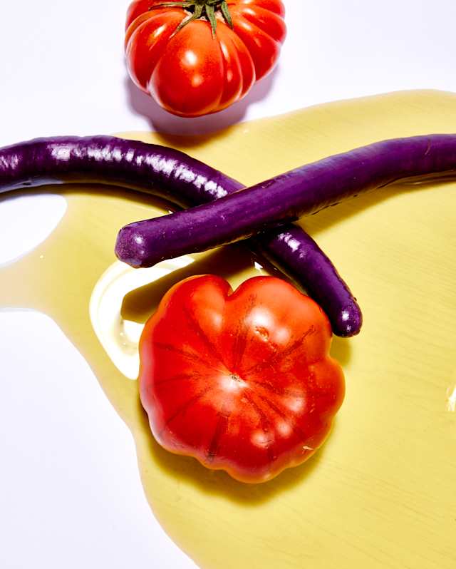 Close-up of two thin Chinese eggplants crossing over on a plate shiny, ripe beef tomatoes above and below, in olive oil.