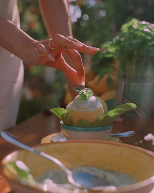 Nara Smith carefully adds a leaf garnish to the top of a lemon and basil sorbet served in the half-fruit, seen close-up.
