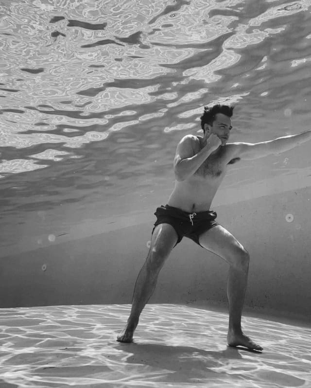 Nicholas Hoult, photographed by Greg Williams in black and white underwater as he stands on the pool bottom in a boxing pose.