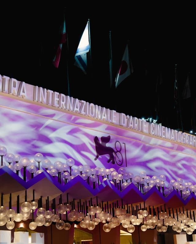 A purple cinema awning, glowing with white ripples and dripping with globe lights, advertises the eighty-first film festival.