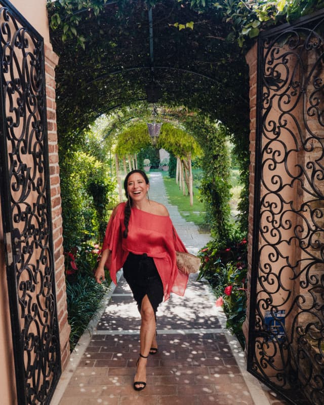 Barbara Maniacco, Guest Relations Manager, strolls from the gardens to the hotel in a red, diaphanous off-the-shoulder top.
