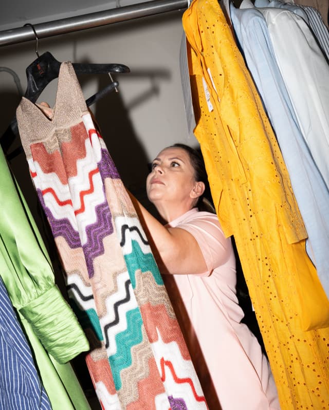 Staff member, Valentina Gentina hangs a laundered long dress with a zig-zag pattern in beige, purple, green, white and red.