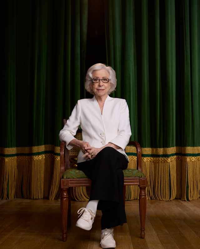 A group of six people, four adults and two boys, stand closely together smiling for a photo at an indoor event. They are dressed in semi-formal to formal attire, with a dark background behind them.
