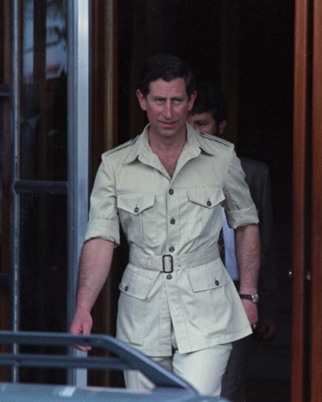 King Charles - then Prince - leaves the hotel in a pale beige safari suit with sleeves rolled up, watched by press and staff.