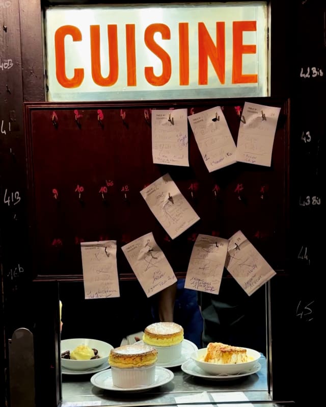Soufflés sit in a dumb waiter pinned with order tickets and with an illuminated sign saying 'Cuisine', taken by Sam Youkilis.