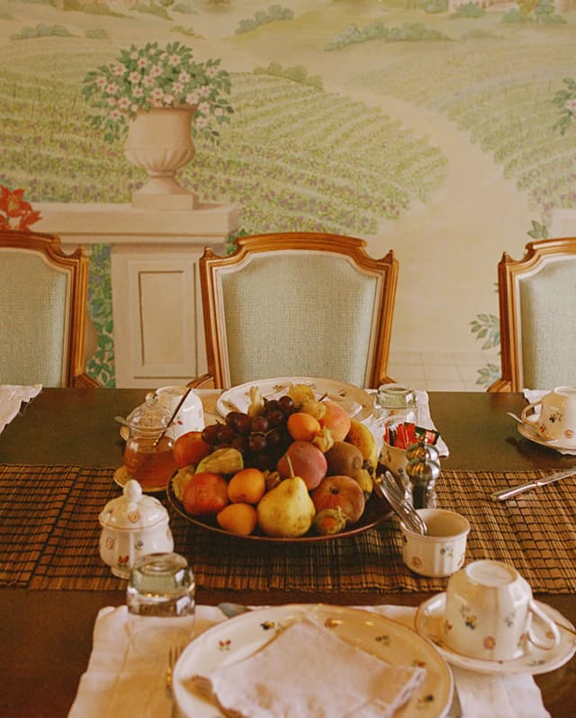 A huge fruit bowl, a honey pot and vintage crockery await Amaryllis's breakfasters at a table in front of a vineyard mural.