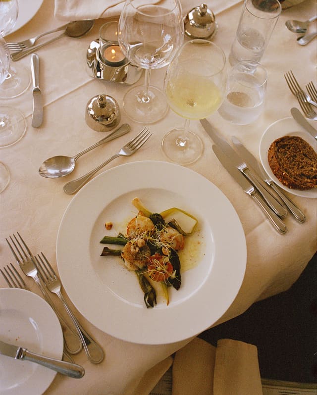 Looking down on a plate of king prawns, greens and buttery sauce at dinner on the Amaryllis, with wine, candles and cutlery.