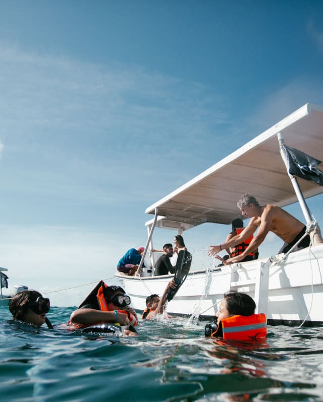 Eye-level view of four divers in the water by two white boats, during a For The Oceans environmental excursion.