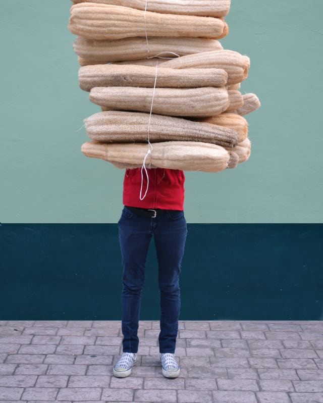 Mexican designer, Fernando Laposse stands by a mint-hued wall, holding a tied bundle of dried luffa, which obscures his face.