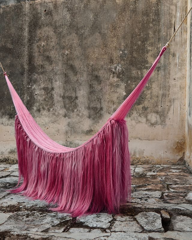 A sculptural hammock with sisal manes, based on a Mayan design, hangs in a stone courtyard, created by Fernando Laposse.