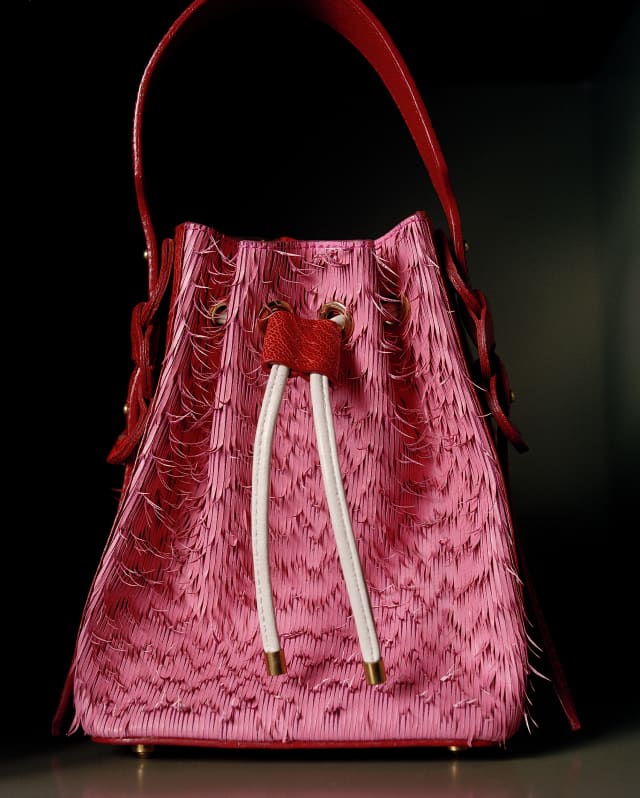 A tasselled pink bag with white pulls and a red shoulder strap by Viviers Studio stands out against a black background.