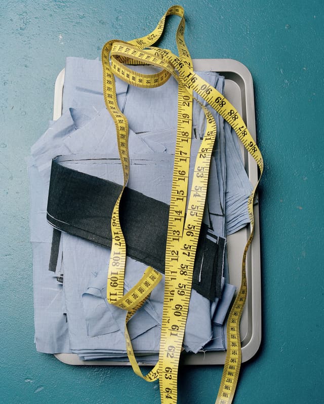A pile of folded blue fabric sits in a metal tray with an unwound yellow tape measure resting on top.