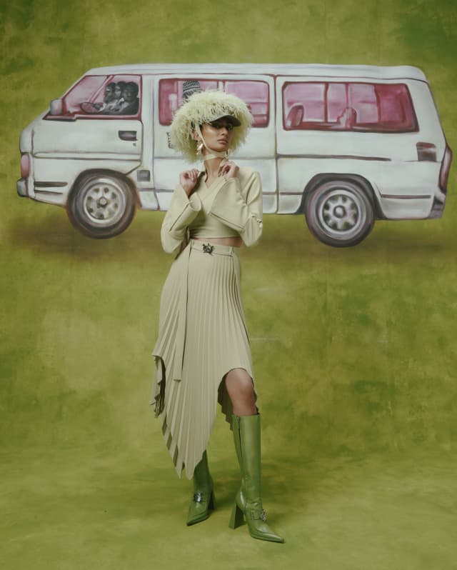 With a graphic backdrop, a model wears a pleated skirt in soft pistachio with a matching top and feather hat by Thebe Magugu.