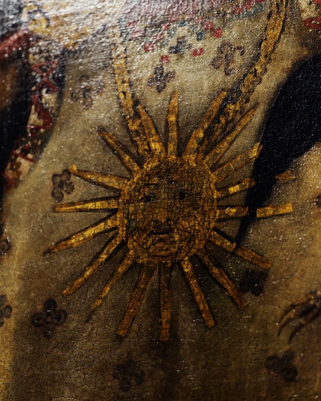 Close-up of a sun with a face, bristling with sunbeams, painted in gold on canvas, in an art detail.