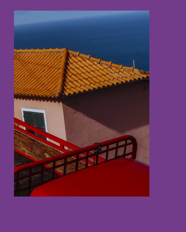 Artistic geometric image of a terracotta-roofed house with soft pink walls and ocean backdrop, seen over red railings.