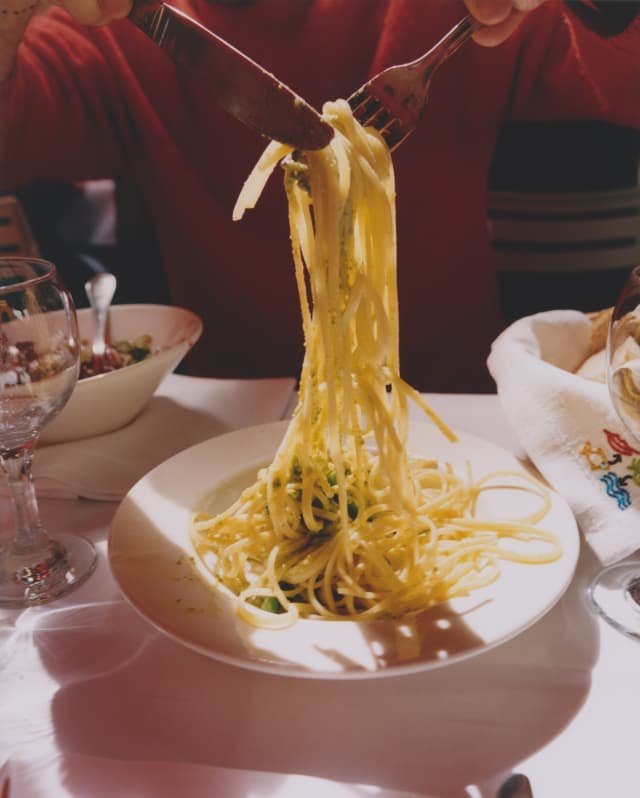 A diner uses a knife and fork to lift some spaghetti al Pesto Genovese from a bowl, in an image from the Liguria cookbook.