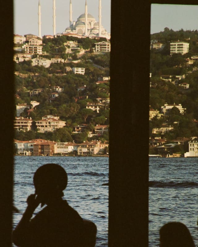 Silhouetted figures stand at tall windows overlooking Haydarpaşa Port and the splendid Çamlıca Republic Mosque on the hilltop.