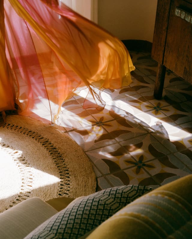 A light breeze through an open window causes a red and orange, diaphanous drape to billow into the living space.