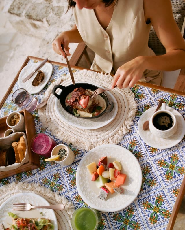 A guest of Casa Mayor tucks into Huevos Rancheros at a breakfast table with topped toast, coffee and a bowl of diced fruits.