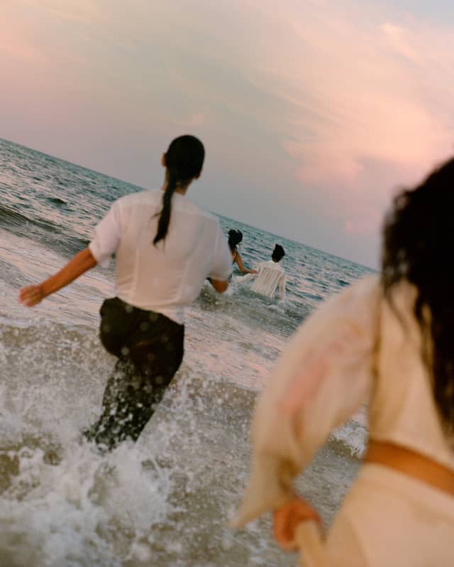 Guests run fully-clothed into the ocean froth at sunset, following a Temazcal ritual, seen from behind on the diagonal.