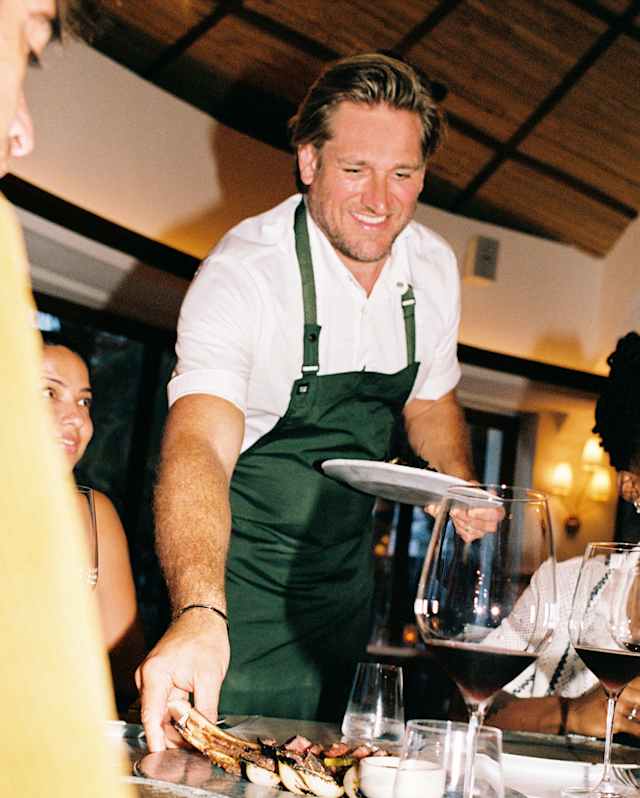 Smiling, Chef Curtis Stone delivers a plate of grilled, wood-fired ribeye steak to a table of diners at Woodend.