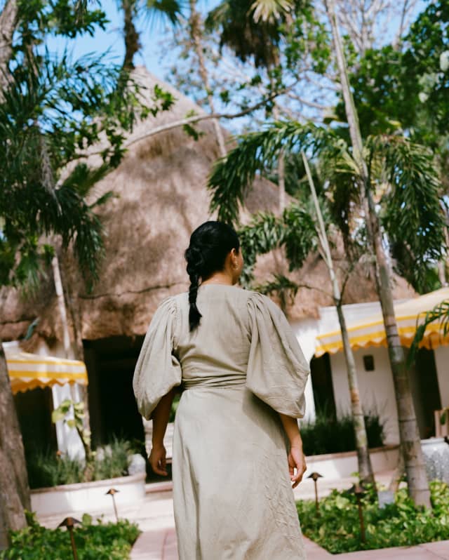 In sage uniform dress, a female member of staff with dark hair in a plait walks towards the hotel lobby, seen from behind.