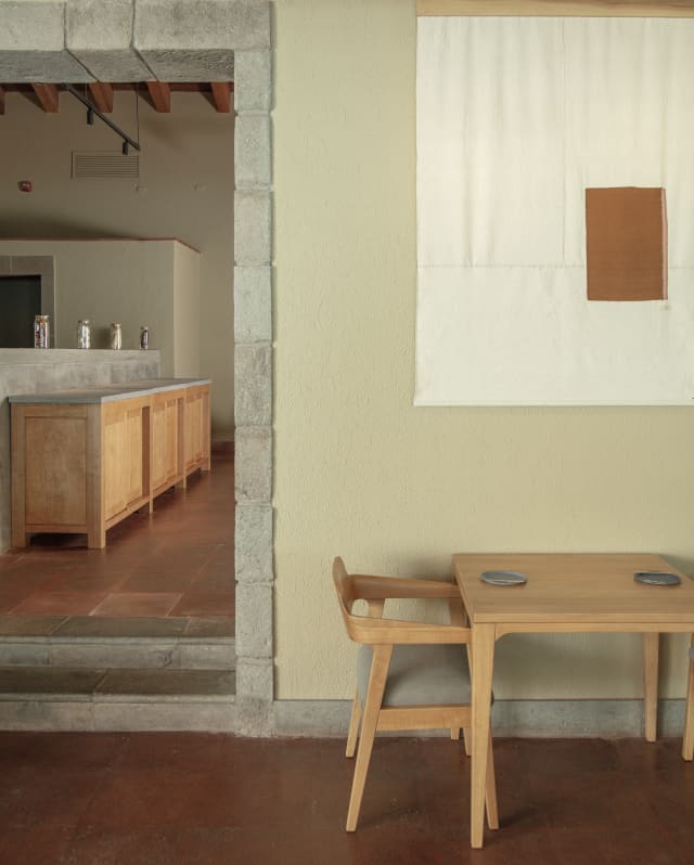 In Mauka's interior, with natural décor, a table for two sits below a wall hanging by a doorway to another restaurant area.
