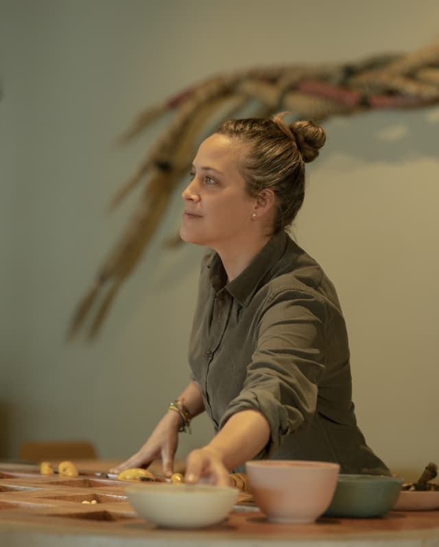 Chef Pía León, hair tied in a bun and wearing a khaki shirt with sleeves rolled up, reaches for a bowl in Mauka Restaurant.