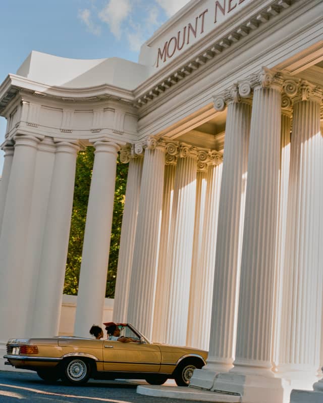 Two guests in a yellow convertible car pass through the spectacular, tall columns of the Mount Nelson Hotel's Royal Gateway.