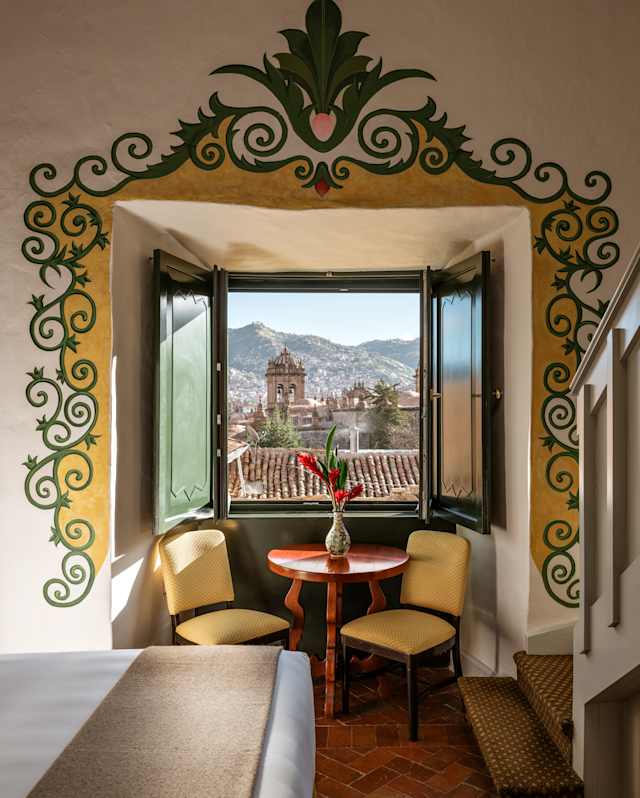 In a Junior Suite bay window with an illustrated border, a red table and two yellow chairs enjoy breathtaking rooftop views.