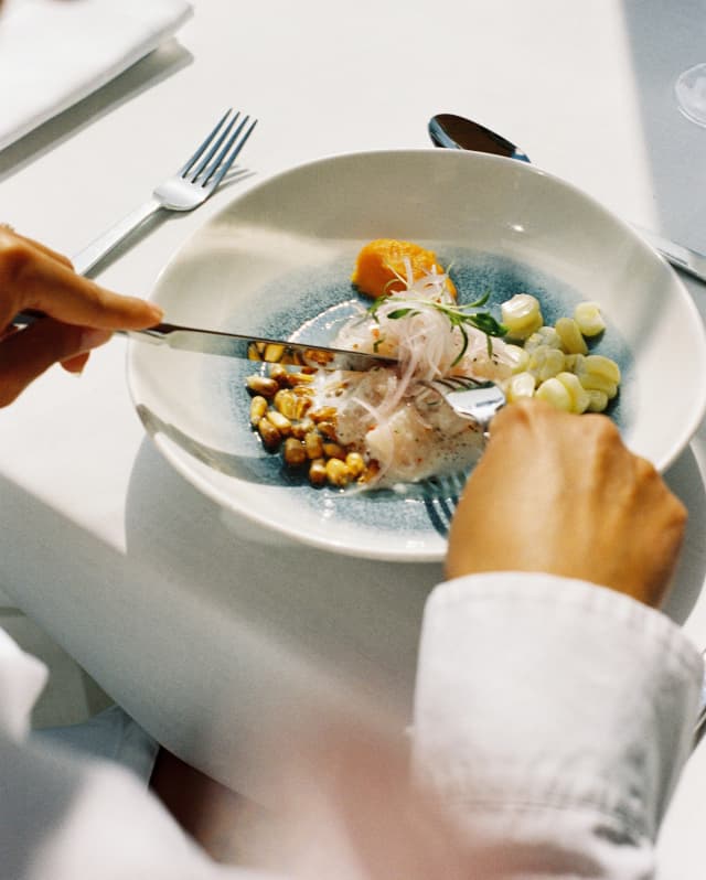 A guest cuts into a classic ceviche dish at Tragaluz, with onions, sweet potato and fresh corn, seen over a diner's shoulder.
