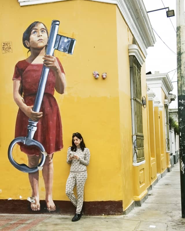 A woman looking at her phone, leaning against a yellow wall in Barranco, Lima