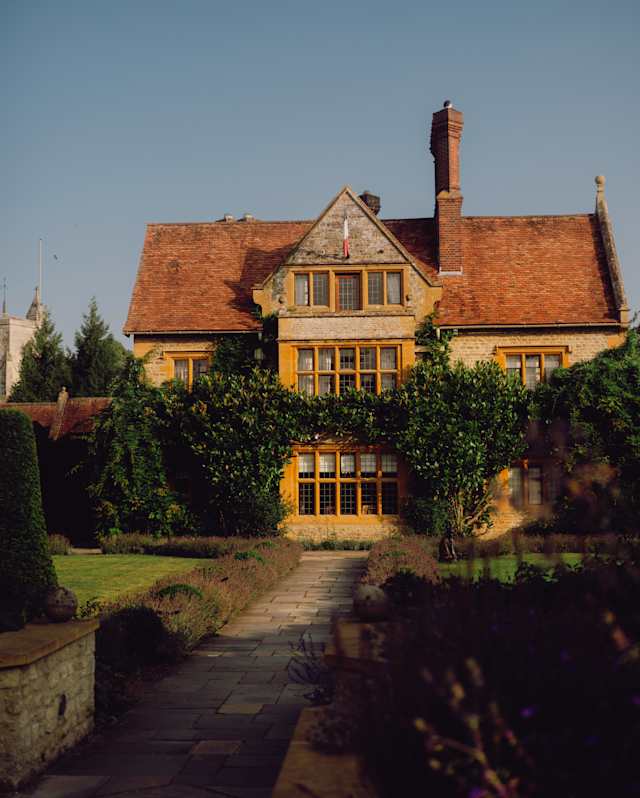 The beautiful honey stone and terracotta roof of Le Manoir glows in late sun, in a stunning view from the gardens.