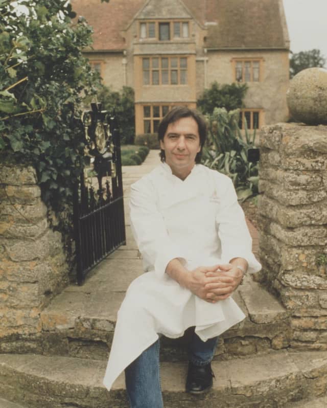 An image of a young dark-haired Chef Raymond Blanc on the garden steps of Le Manoir Aux Quat'Saisons, in jeans and whites.