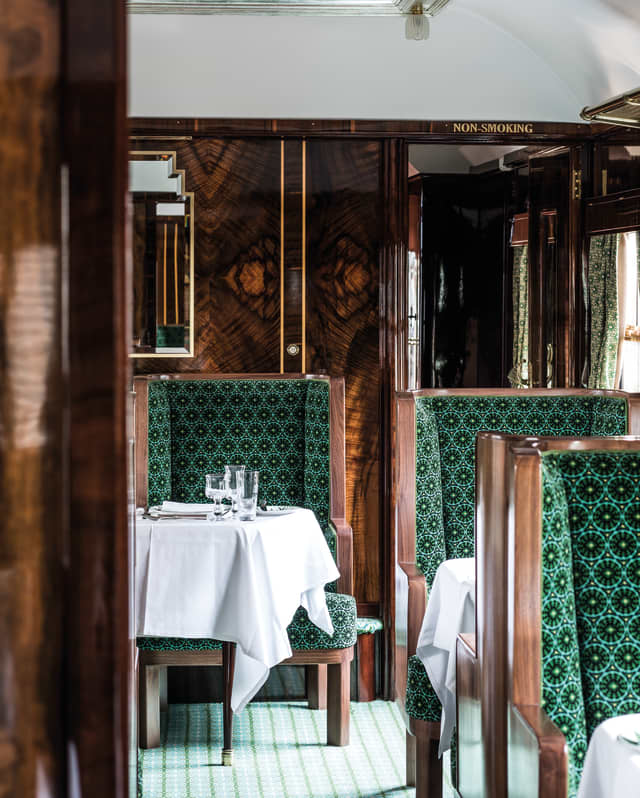 French polished wood panelling on walls and chair frames catches the light. Gilt framed mirrors feature zigzag art deco edges