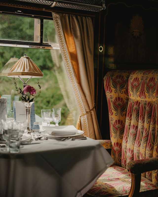 Soft window light falls on a dining table laid for guests and a padded, Art Deco beige and red chair, in a Gwen Car detail.