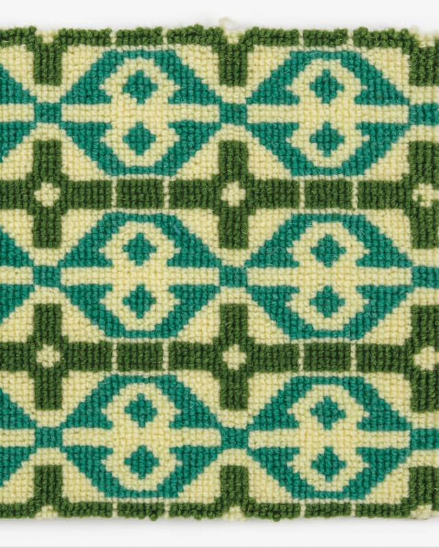 The carpet features a cream background with a cream figure of 8 within a turquoise diamond and dark green square frames