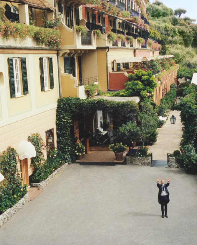 The concierge waves from the hotel's courtyard, surrounded by lush wall-hugging ivy and a long hedge of pink roses