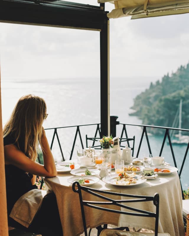 In the corner of the La Terrazza terrace, a woman sits at a table of finished plates and empty glasses, gazing at the view.