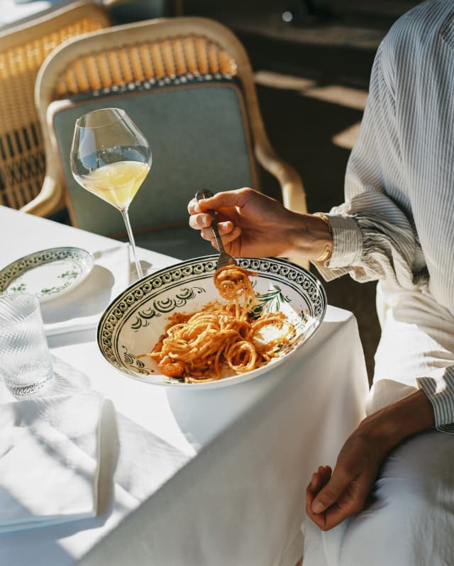 Sunlight falls on a dining table where a guest enjoys spaghetti with rich tomato sauce with a drink at Splendido Grill.