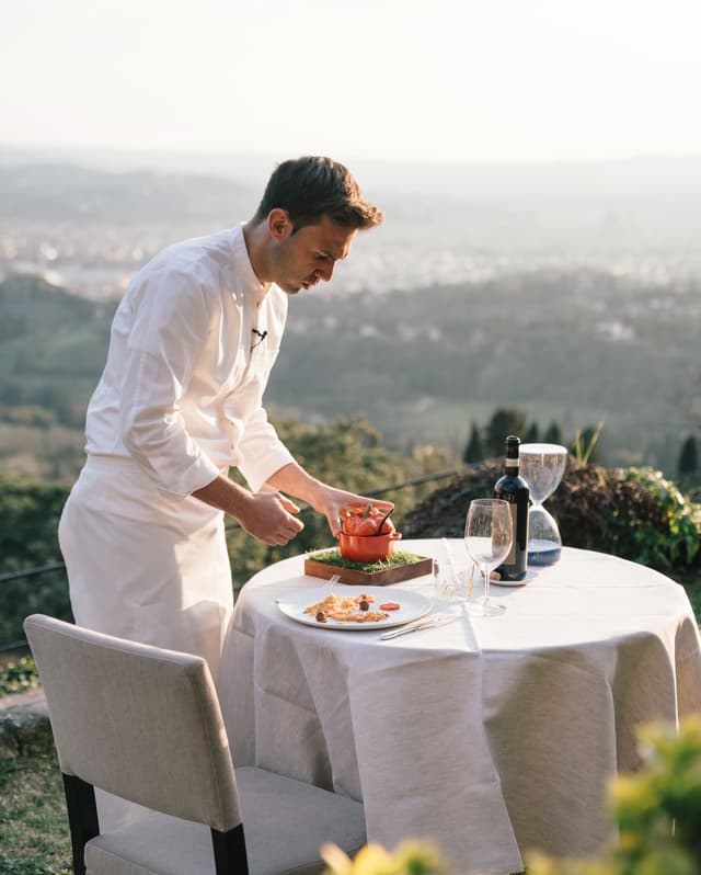 Executive chef, Alessandro Cozzolino, prepares a dish at a table on the garden terrace overlooking views of Florence
