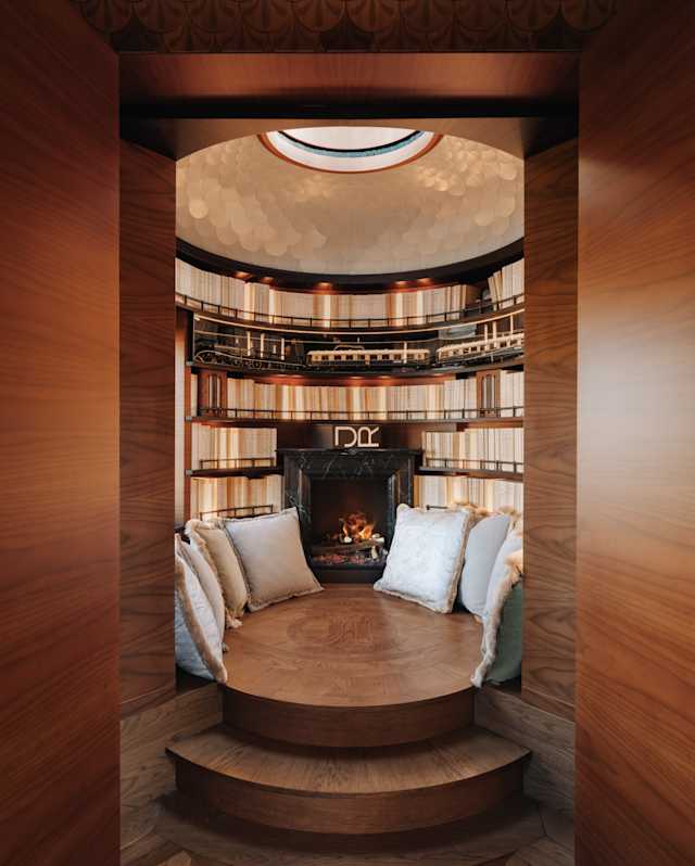 View into L'Observatoire's library-tearoom where floor cushions are propped either side of a fire, surrounded by bookshelves.