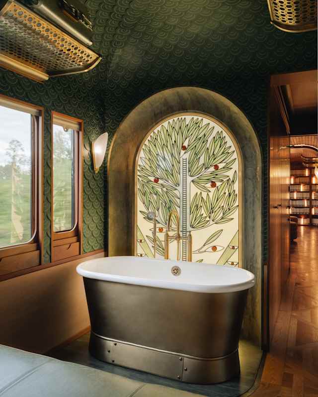 A stained glass depiction of a tree, by Franz Mayer of Munich, rises behind a brass freestanding bathtub with white enamel.