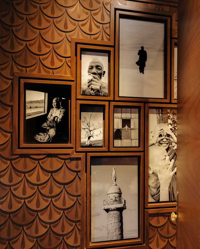 Seven of JR's photographs from his travels are seen, set in frames in a wall of repeat scallop-patterned marquetry.