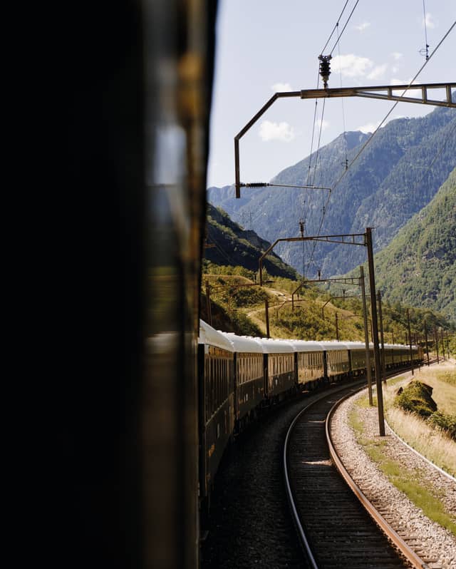 Royal blue and cream exterior of a luxury train curving through a Swiss valley