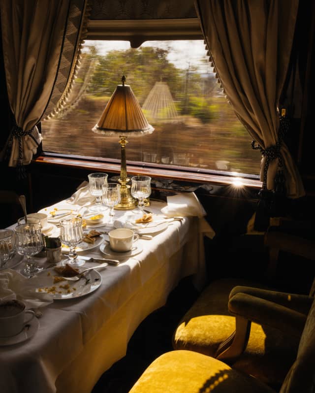 Sunlight settles on gold velvet seats at a window table, covered with finished plates and glasses in L'Oriental dining car.