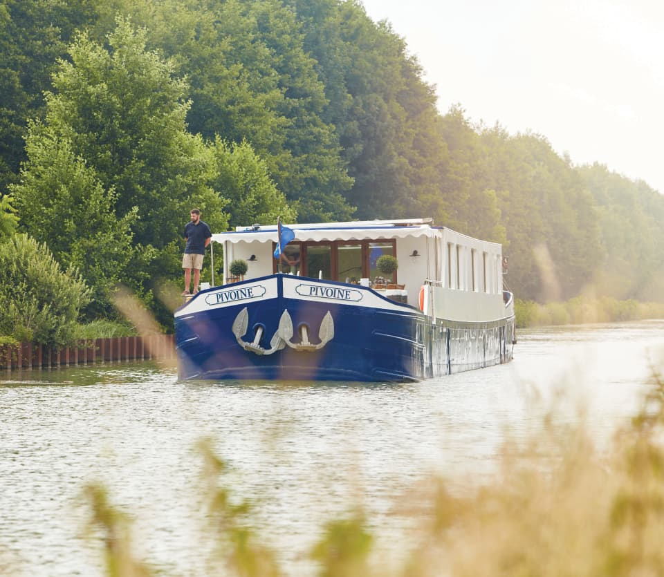 Blue bottomed luxurious river barge sailing along a tree-lined river