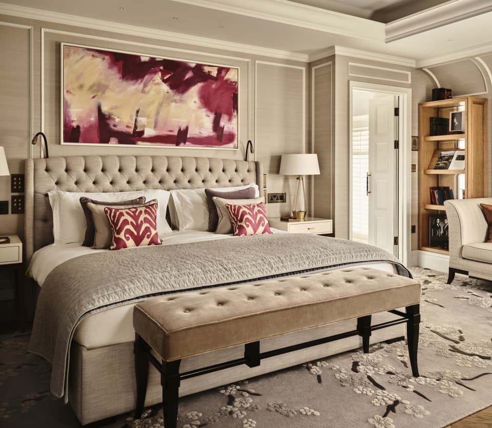 View of the luxury Penthouse bed where beige upholstery and cream bedding pairs with red hints in cushions and wall art.